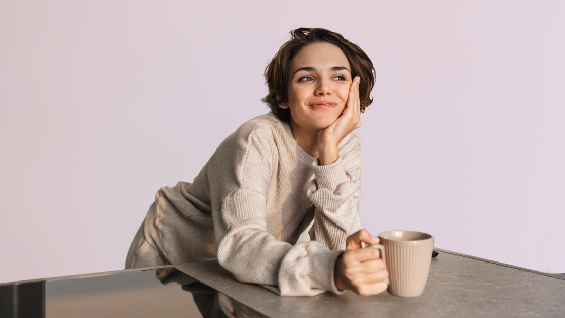 Une femme souriante prend entre ses mains une tasse. 