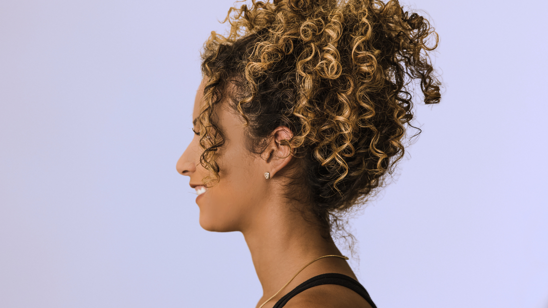 Une femme avec les cheveux bouclés qui sourie sur un fond violet clair.