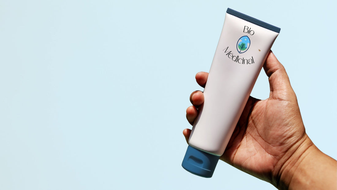 Une main qui soutien une crème solaire sur un fond bleu clair.